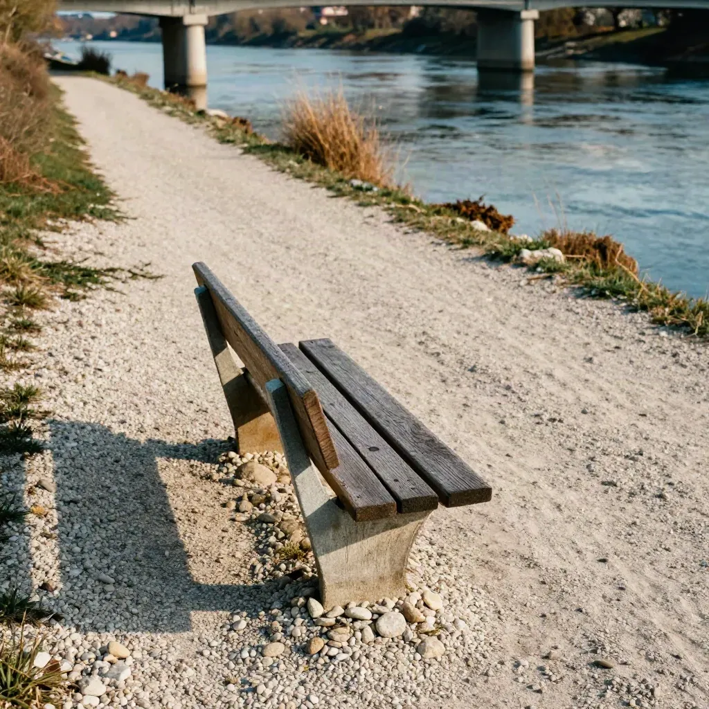 Flache Radroute am Fluss mit Rastbank, Kiesufer und Brückenpfeilern im warmen Licht